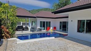 A modern house with a swimming pool, outdoor furniture, and a view of the surrounding greenery.