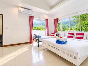 A hotel room with a large bed, a separate chair, a window with a view of greenery, and an air conditioning unit. - Phikun Private Pool Villa (Chalong)