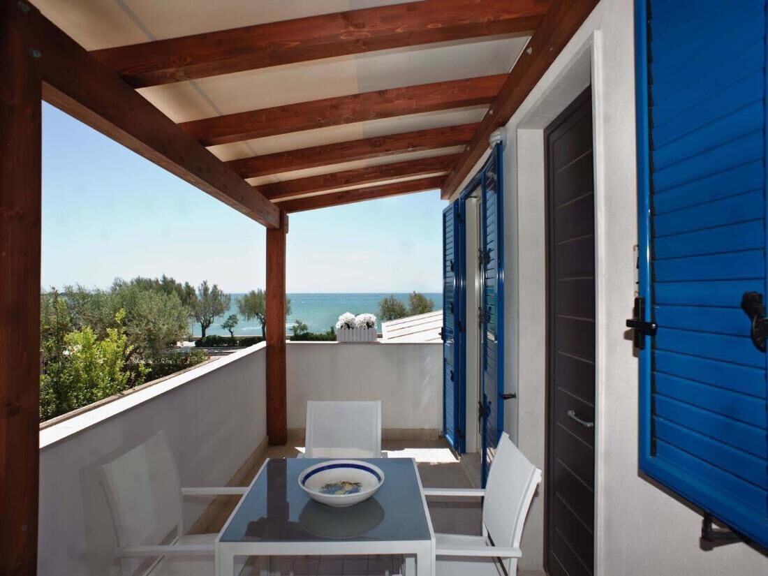 A balcony with a table and chairs, overlooking a scenic view of the sea and greenery.