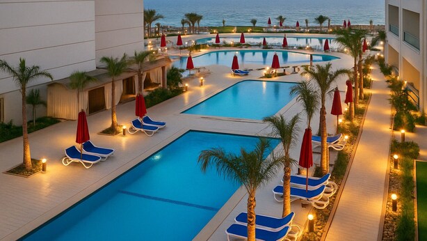 A pool area with multiple pools, lounge chairs, and umbrellas, surrounded by palm trees and a view of the ocean.