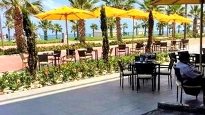 An outdoor seating area with yellow umbrellas, palm trees, and a view of the sea.
