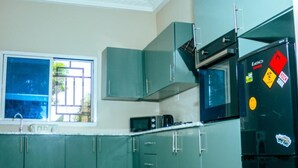 Una cocina con armarios verde azulado, un refrigerador negro y una ventana con vistas a la vegetación.