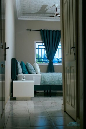 A bedroom with a bed, a bedside table, and a window with curtains.