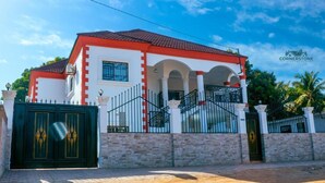 Una casa de dos pisos con techo rojo, paredes blancas y un portón negro.