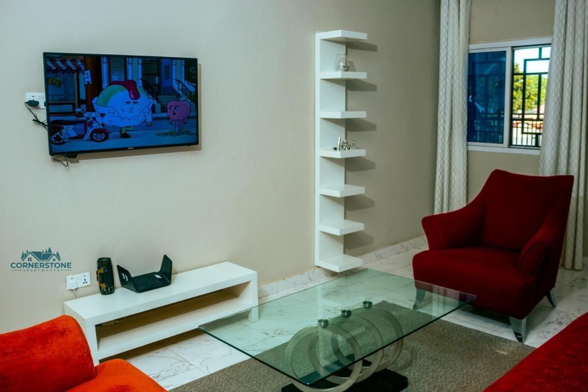 Ein modernes Wohnzimmer mit Flachbildfernseher, einem Glastisch, einem roten Sessel und einer weißen Regaleinrichtung.