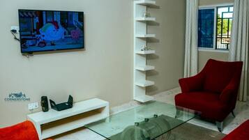 Ein modernes Wohnzimmer mit Flachbildfernseher, einem Glastisch, einem roten Sessel und einer weißen Regaleinrichtung.