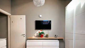 Ein modernes Zimmer mit einem flachbildfernseher an der Wand, einem hölzernen Regal mit Zimmerpflanzen und einem weißen Stauraum mit Schubladen.