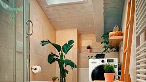 Ein kleines Badezimmer mit Duschkabine, Toilette, Waschmaschine und einem Holzstuhl.