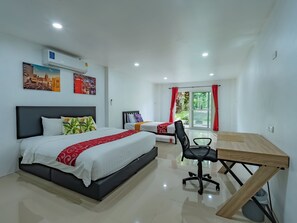 Een hotelkamer met twee bedden, een bureau, een stoel en uitzicht op groen buiten het raam.