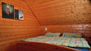 Une chambre dans une cabane en bois, avec un lit, deux tableaux accrochés au mur et un plafond en bois.