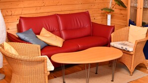 Une pièce chaleureuse avec un canapé en cuir rouge, des fauteuils en osier et une petite table en bois.