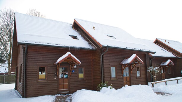 Une cabane en bois, dont le toit est recouvert de neige, et un chemin de briques menant à l’entrée.