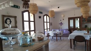 A dining area with a buffet setup, a sofa, and a table with a vase of flowers. - Room in B&B - "note di Stelle" Resort in Marrubiu (Marrubiu)