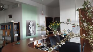 A modern office with a curved wooden desk, a black office chair, a clear glass pendant light, and a vase with white flowers. - Room in B&B - "note di Stelle" Resort in Marrubiu (Marrubiu)