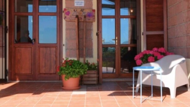 A brick building with a wooden door and windows, a tiled patio, a white chair, and potted plants. - Room in B&B - "note di Stelle" Resort in Marrubiu (Marrubiu)