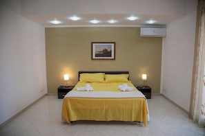 Une chambre d’hôtel avec un lit, deux tables de chevet, un tableau au mur et un climatiseur.