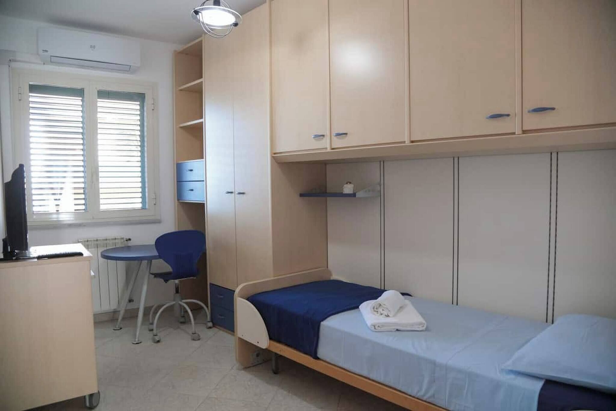 A bedroom with a single bed, a desk, a chair, and built-in wardrobes.
