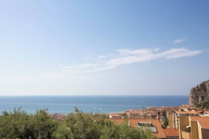 Une ville côtière aux bâtiments aux toits de tuiles rouges, dominée par une falaise imposante, et offrant une vue dégagée sur la mer.