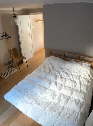 A bedroom with a large bed, a wooden headboard, a white door, a chair, and a hanging light fixture.