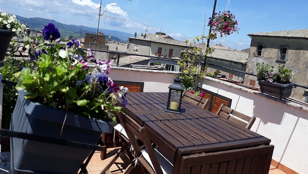 Een houten tafel met stoelen op een terras, met bloempotten en hangende bloemen.