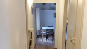 Een smalle gang met betegelde vloer die leidt naar een eetgedeelte met een tafel en stoelen.