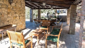An outdoor patio with stone walls, wooden furniture, and a table with chairs.
