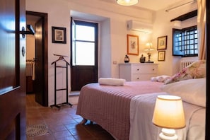 A bedroom with a bed, a bedside lamp, a radiator, a window, and a door. - Villa Cefalù Private Pool (Cefalù)