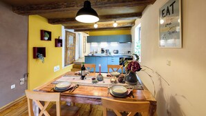 Un comedor con una mesa de madera dispuesta para cuatro personas, una lámpara colgante y una cocina al fondo.