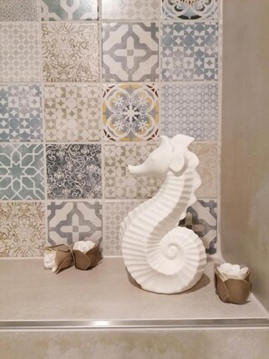 A bathroom with a tiled wall featuring various geometric and floral patterns. A white seahorse sculpture is placed on the floor. - Ackerburgerhof Ballstrase 18 (Quedlinburg)