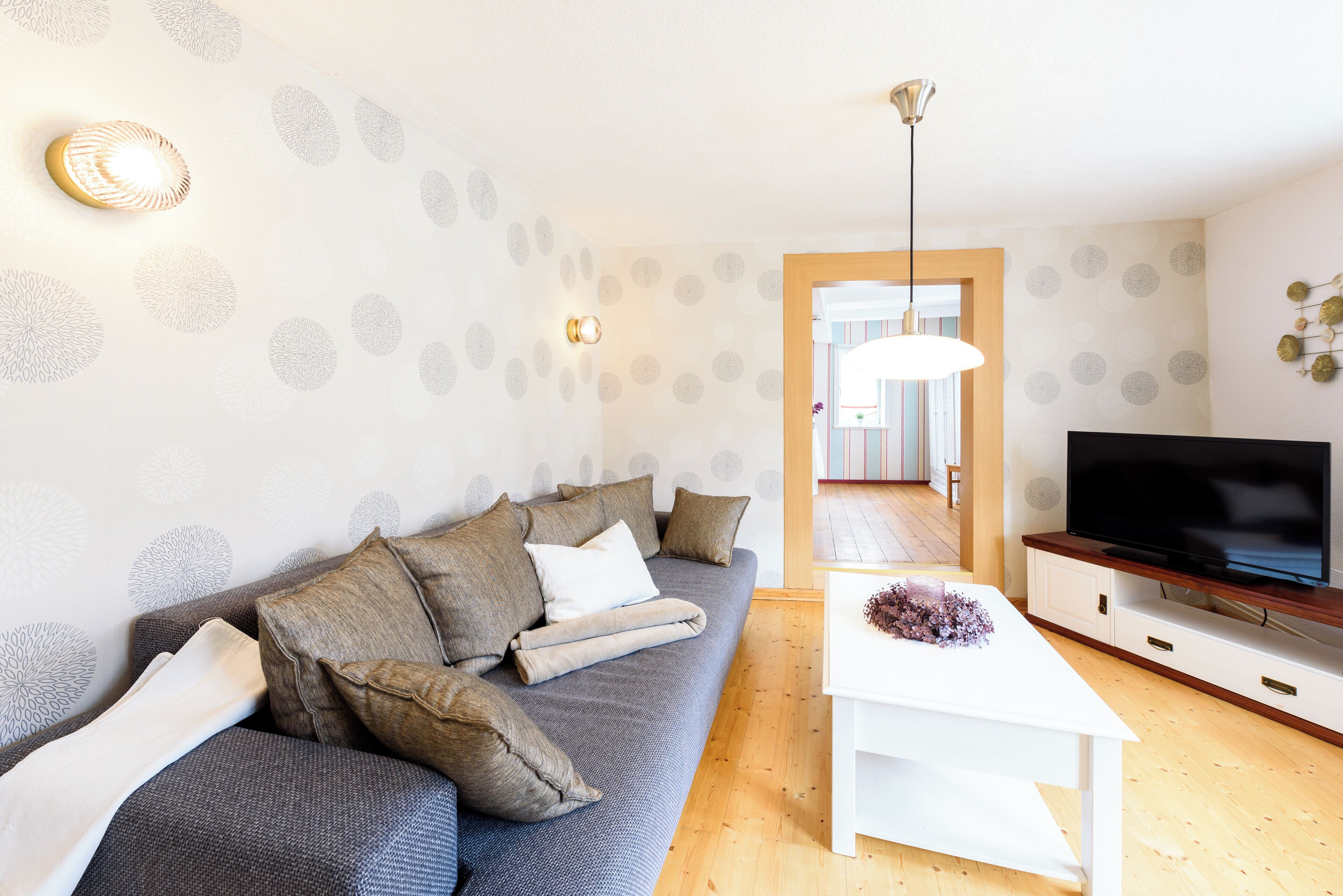 Ein modernes Wohnzimmer mit grauem Sofa, weißem Couchtisch und einem Flachbildfernseher auf einem Holzboden.