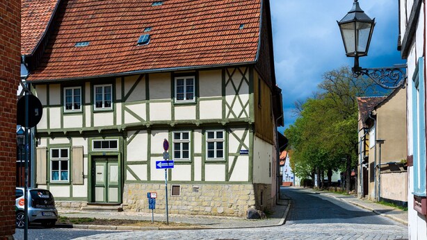 Una calle adoquinada con edificios tradicionales de entramado de madera, un farol y un cielo azul despejado.