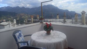 A balcony with a table and chairs, overlooking a mountainous landscape. - Ravello for You Casa Gallo (Ravello)