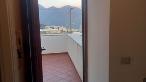 An open door leading to a balcony with a tiled floor and a view of buildings and mountains in the distance. - Ravello for You Casa Gallo (Ravello)