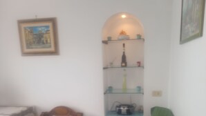 A living room with a green sofa, a wooden chair, a small table, and a shelf with various items. - Ravello for You Casa Gallo (Ravello)