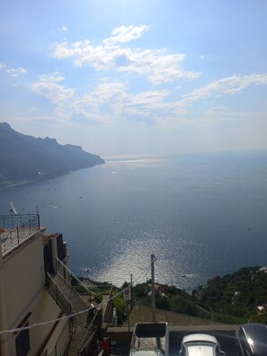 A coastal view from a high vantage point, overlooking a calm sea with boats, a clear sky, and a hilly landscape. - Ravello for You Casa Gallo (Ravello)