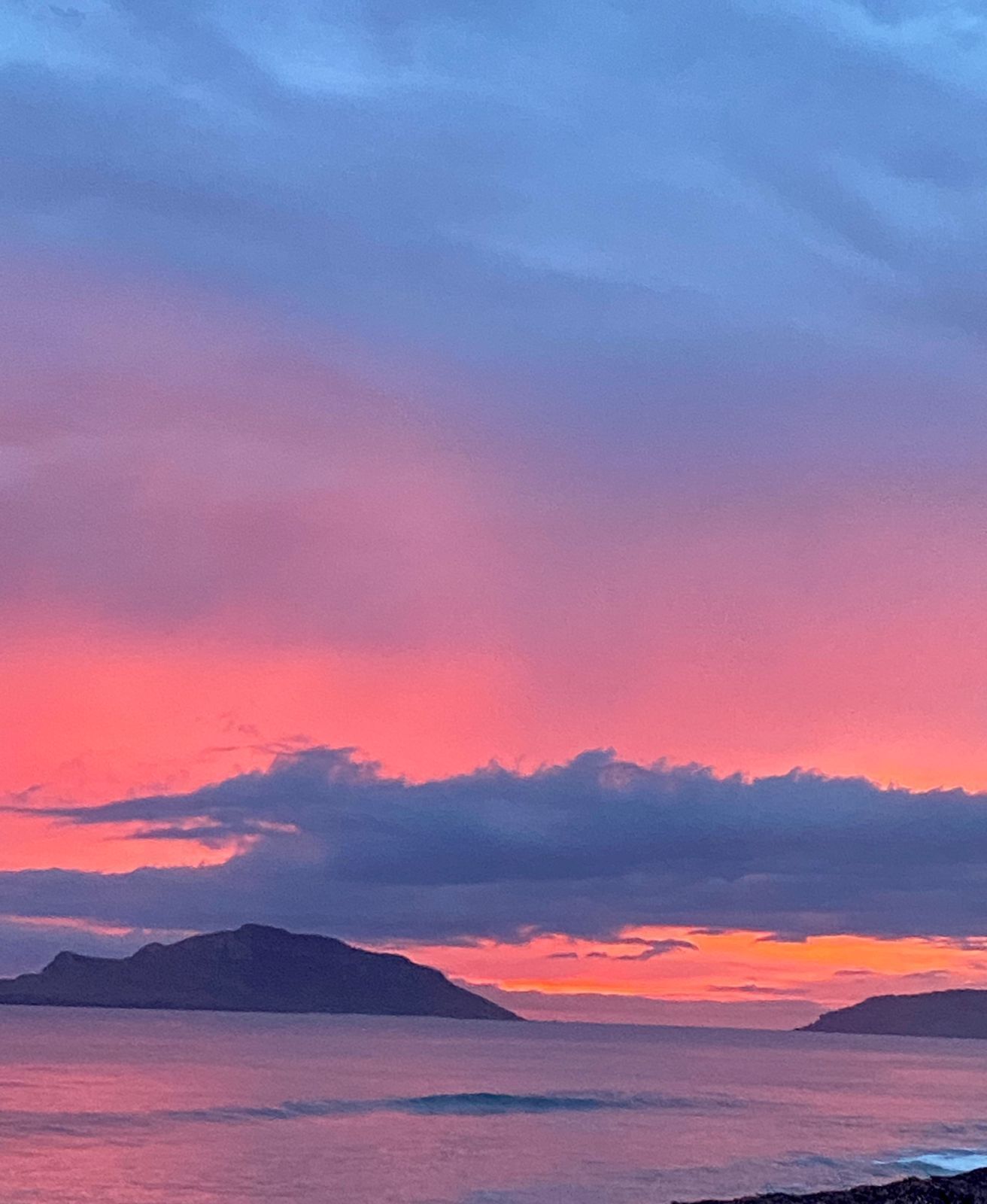 A sunset over a calm sea with distant landforms.