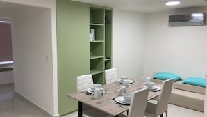 A dining area with a wooden table set for four, white chairs, and a green shelving unit against the wall. - Room-appartment Rodolfo Historical Centr (Mazatlán)