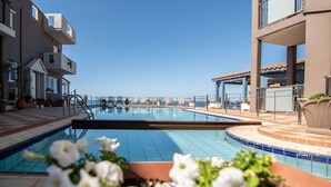 A pool area with a clear view of the ocean, surrounded by modern buildings with balconies. - Room in Guest Room - Girogiali Beach Hotel (Chania)