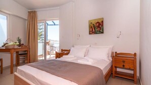 A hotel room with a bed, a desk with a basket of fruit, a chair, and a view of the sea through a sliding door. - Room in Guest Room - Girogiali Beach Hotel (Chania)