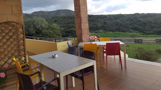 A terrace with a table and chairs, a view of green hills, and a cloudy sky. - Room in B&B - "note di Stelle" Resort in Marru (Marrubiu)