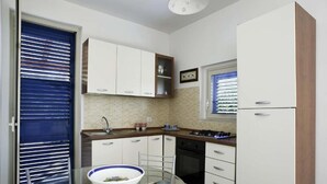 A compact kitchen with white cabinets, a glass dining table, and a blue-framed window. - Dolce Mare 1 - Ground Floor With Garden (Modica)