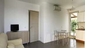 A modern living room with a sofa, a TV, and a dining area with chairs and a table. - Dolce Mare 1 - Ground Floor With Garden (Modica)