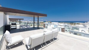 A rooftop terrace with white outdoor furniture, a glass balustrade, and a clear view of the sea. - Protaras Olivine Villa Ol9 (Paralimni)