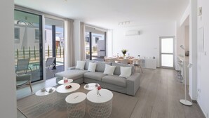 A modern living room with a grey sectional sofa, white round coffee tables, and a glass sliding door leading to an outdoor area. - Protaras Olivine Villa Ol9 (Paralimni)