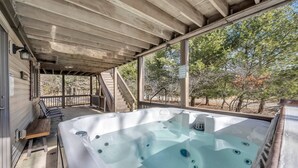 Un espacio al aire libre techado con un jacuzzi, terraza de madera y una escalera que lleva a un edificio.