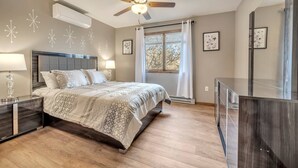 Un dormitorio con cama, mesitas de noche, ventilador de techo y ventana con cortinas.