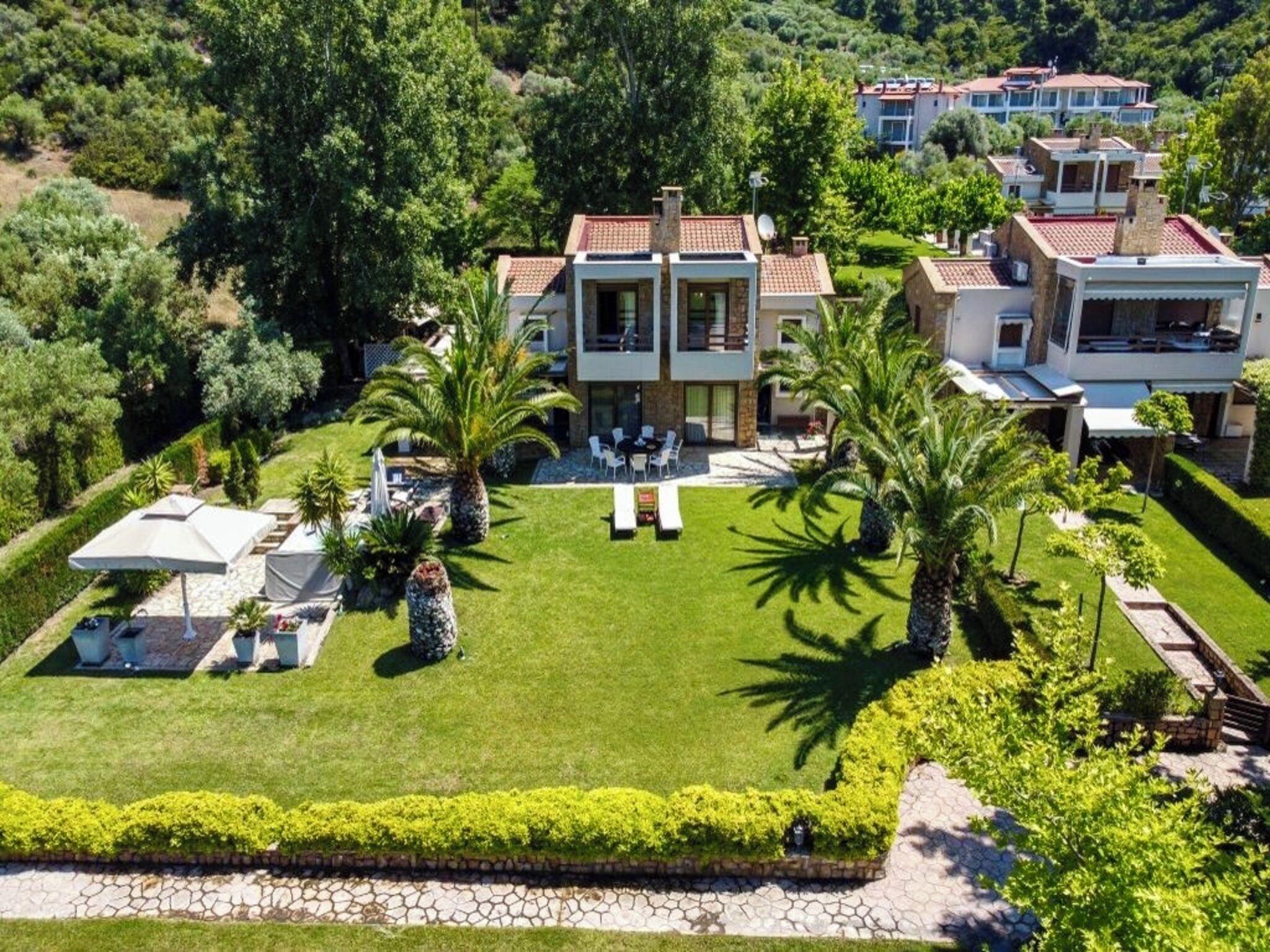 A large, modern villa with a spacious lawn, palm trees, and a pool area.