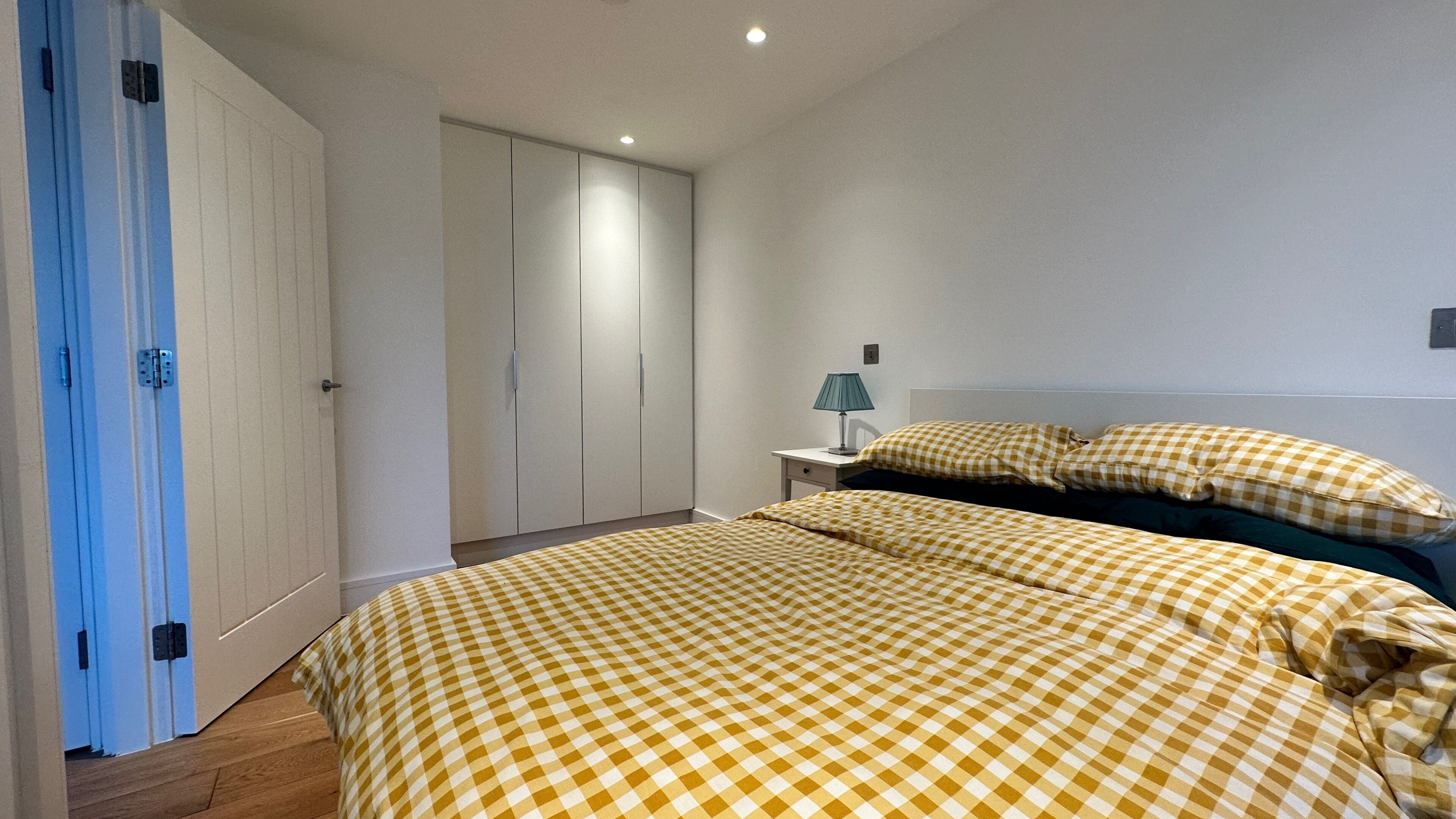 A bedroom with two beds, a wardrobe, a nightstand with a lamp, and a checkered bedspread.