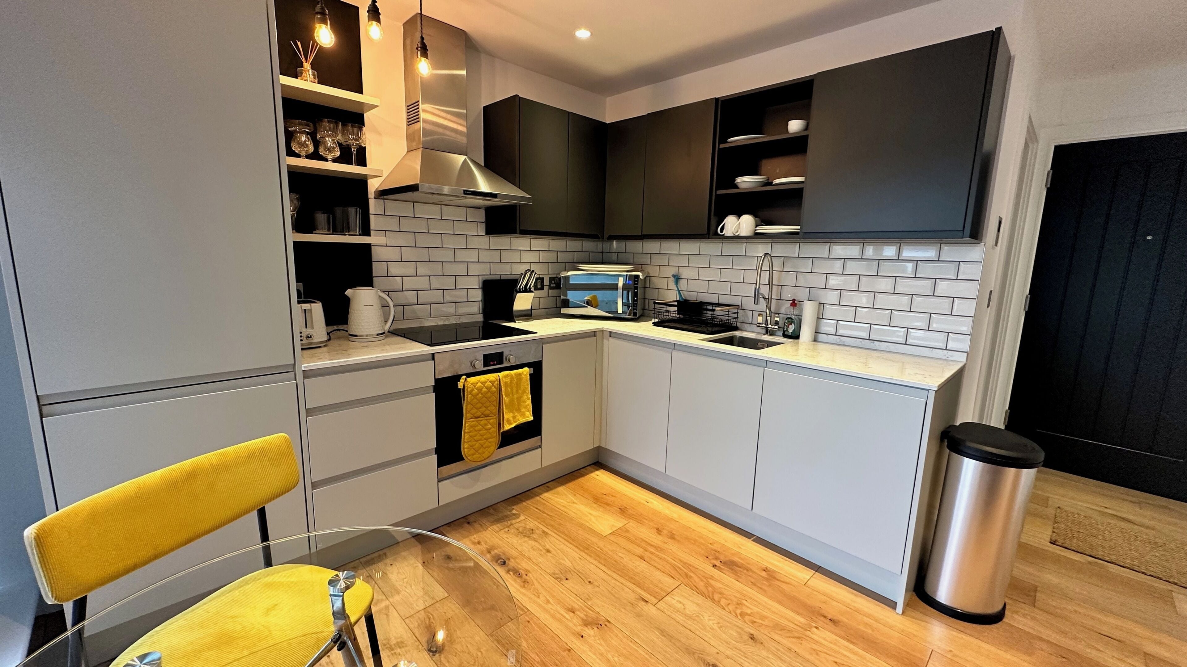 A compact kitchen with modern appliances, a sink, and a yellow chair.