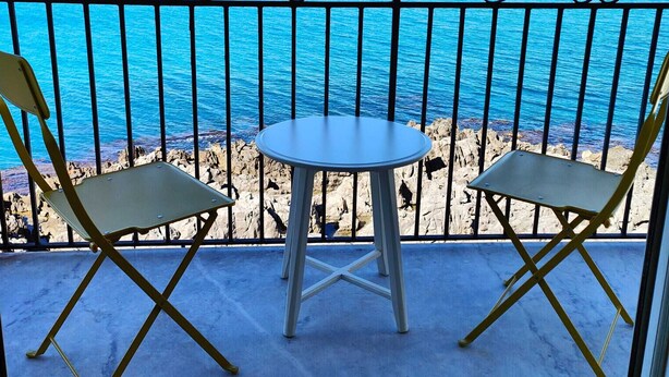 A balcony with two chairs and a table, overlooking a rocky coastline and the sea. - Room-central Room With Balcony And Amazi (Cefalù)